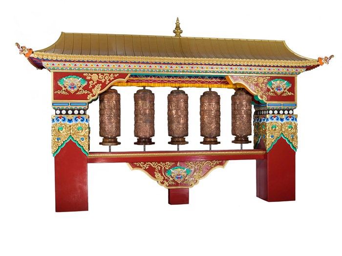 Five bronze cylinders adorned with dense Tibetan script threaded with poles into the centre of a vivid red and gold house-shaped structure.