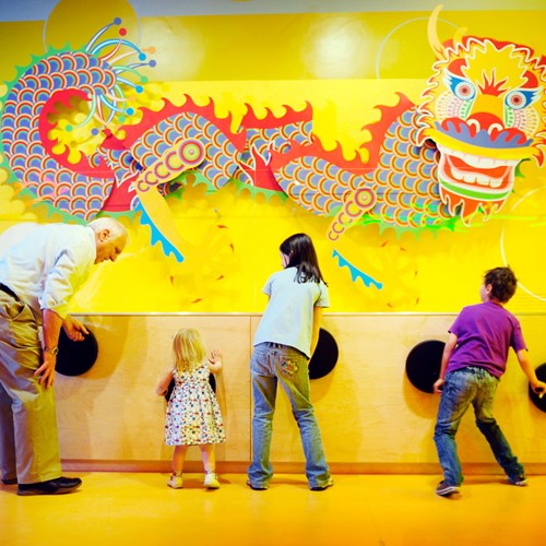Four visitors rotating dials that move an interactive Chinese dragon model on a wall. 