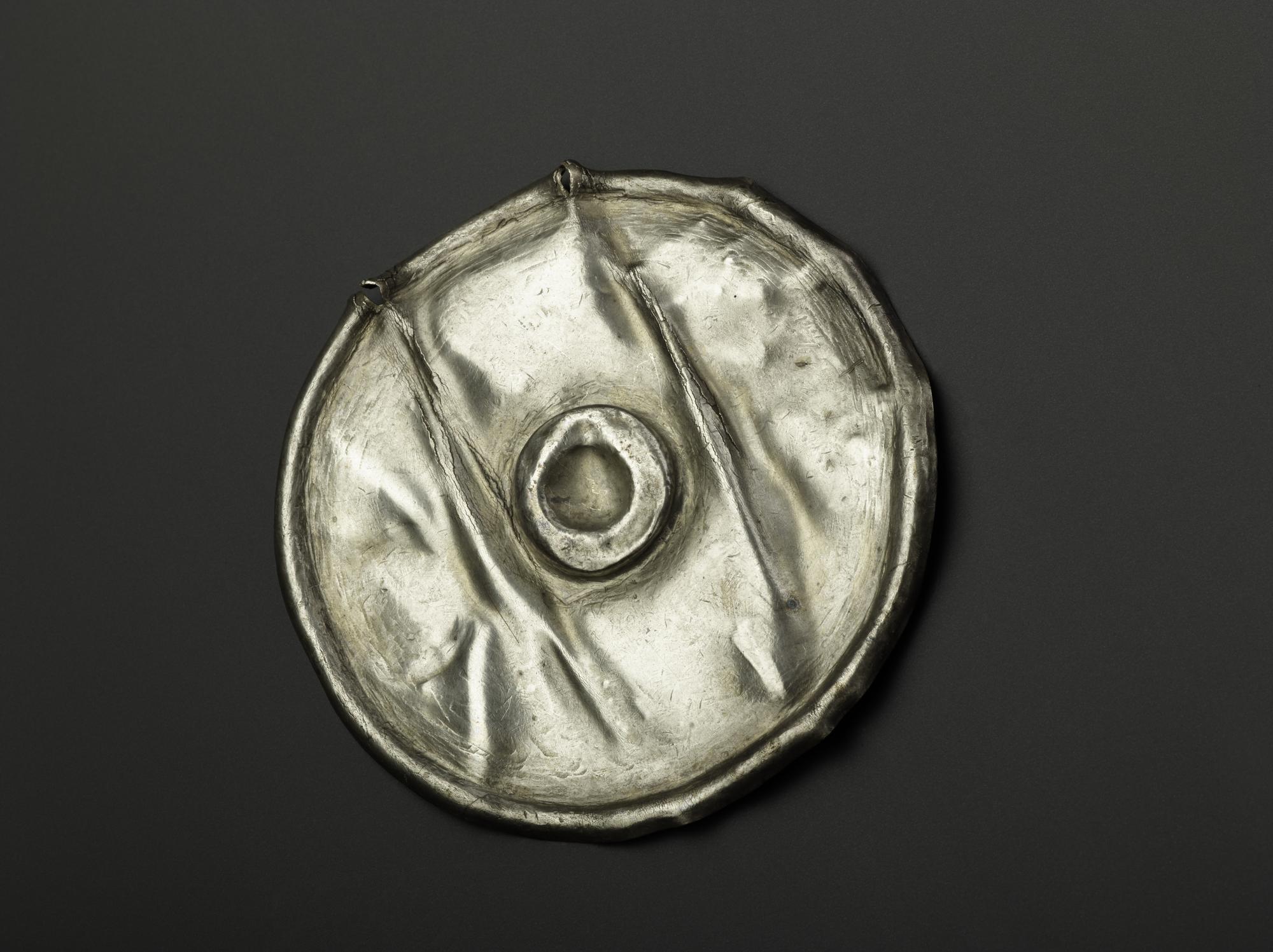Image of Complete silver circular object with central repoussé boss and raised curved rim, from Norrie