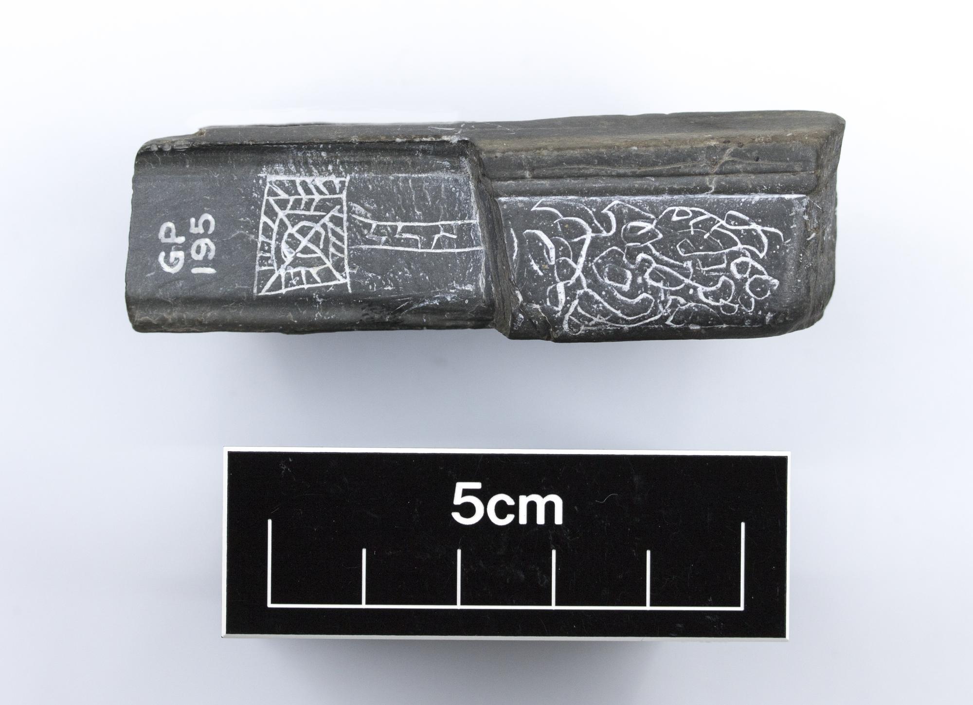 Image of Trial design on a piece of dull green slate, bevelled at one edge and incised with scrolls, from Dunadd, Argyll © National Museums Scotland