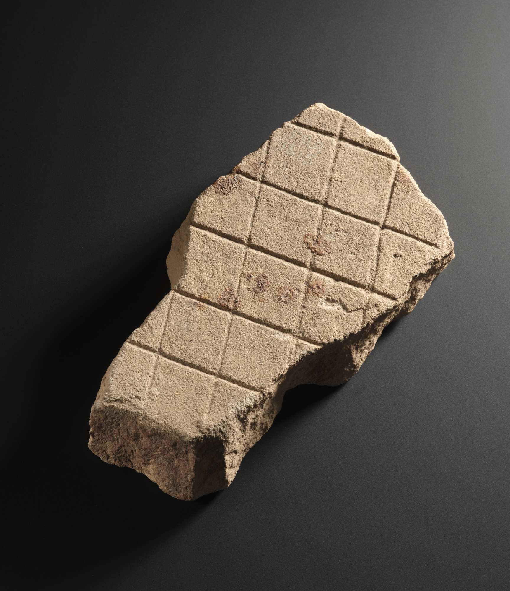 Image of Fragment of a slab of pink sandstone, with shallow diamond broaching, from Newstead, Roxburghshire © National Museums Scotland